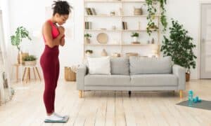 Young woman in activewear checking her weight on a digital scale.